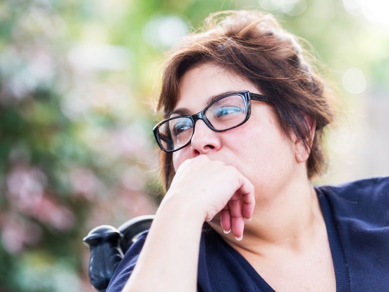 Person with glasses resting their chin on their hand outdoors against a blurred green background