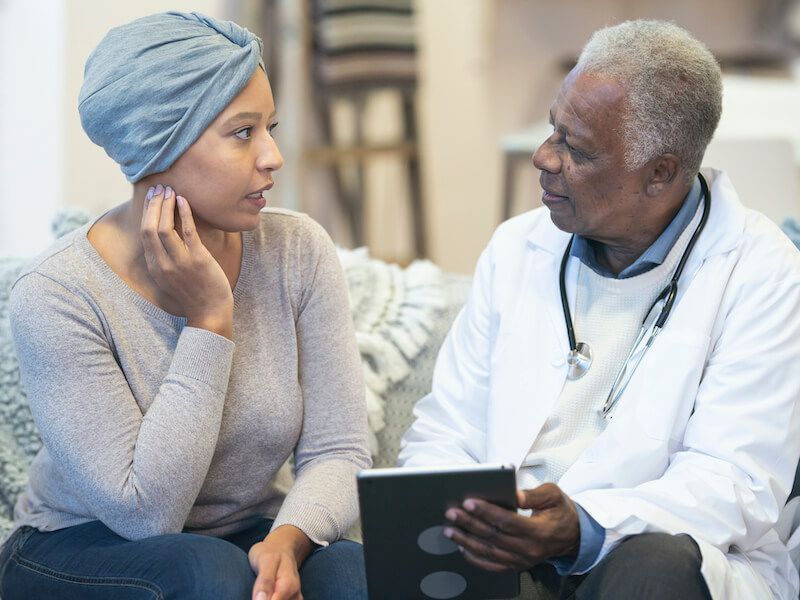 Two people in a clinic discussing care, one holding a tablet and the other wearing a head wrap