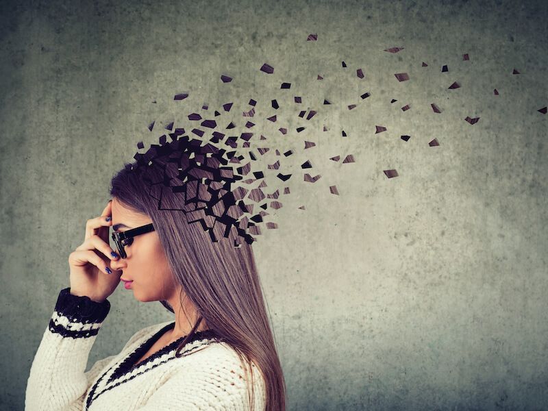 Profile of a woman in glasses, dissolving into scattered black fragments against a gray wall