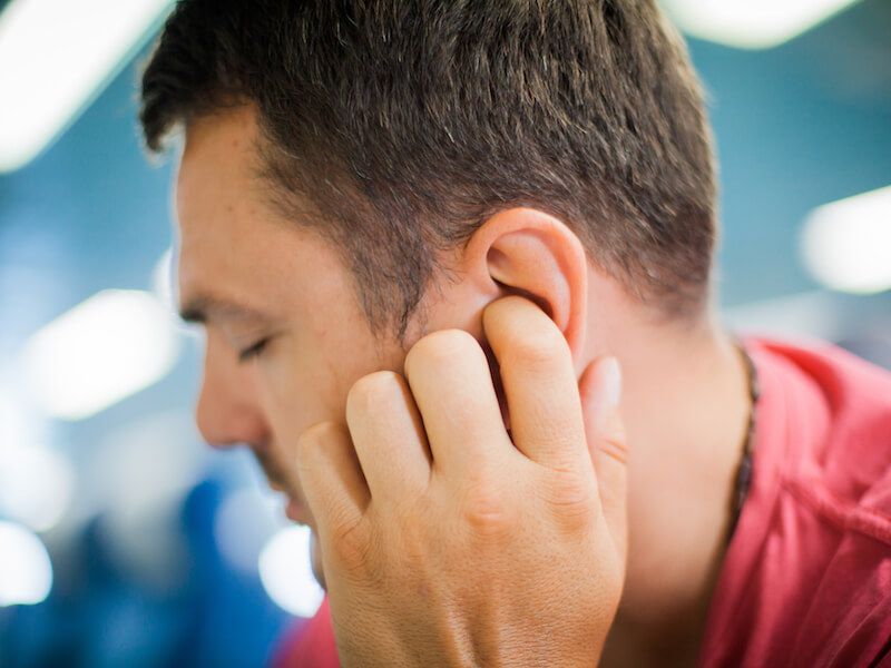 Man holding his ear in a blurred indoor setting, suggesting discomfort or listening closely