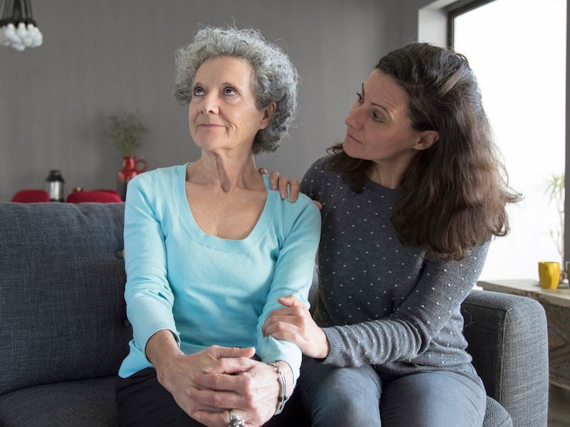 Two women sitting on a couch, one comforting the other in a living room