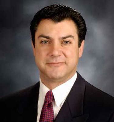 Studio headshot of a man in a dark suit and red tie against a gray background