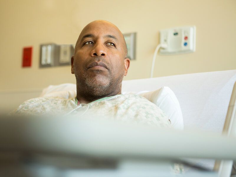 Patient resting in a hospital bed, gazing upward with medical equipment in the background