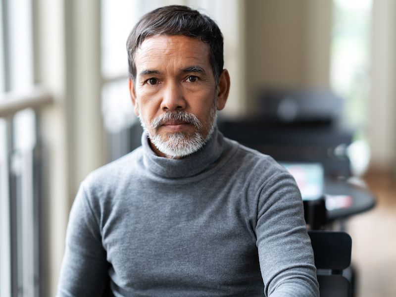 Man in a gray turtleneck seated indoors, looking at the camera with a neutral expression