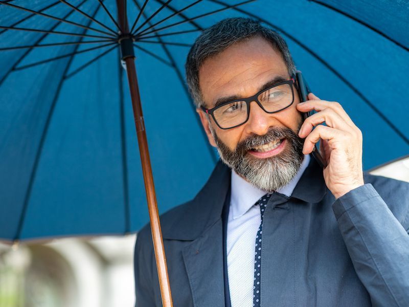 Smiling man in a blue suit holding a phone under a blue umbrella
