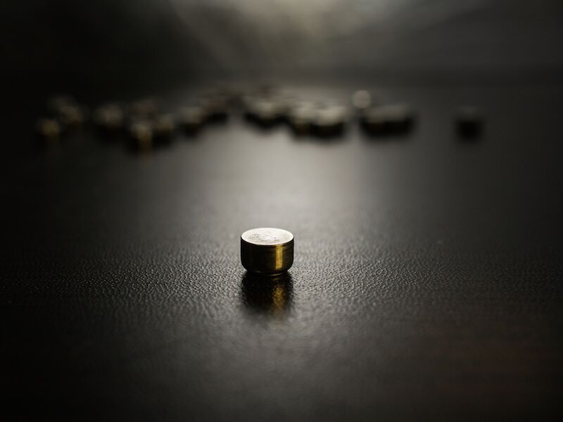 Small metal bullet standing upright on a dark surface with blurred bullets in the background.