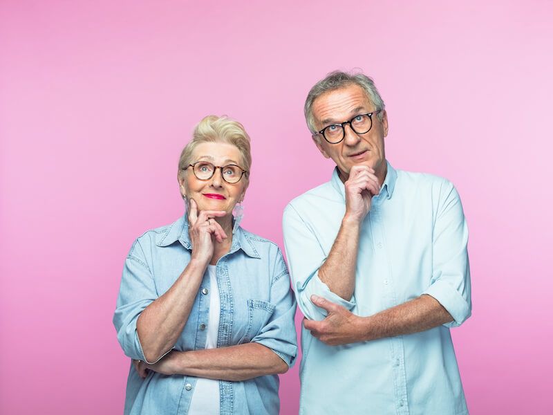 Two people in light blue shirts pose thoughtfully against a pink background.
