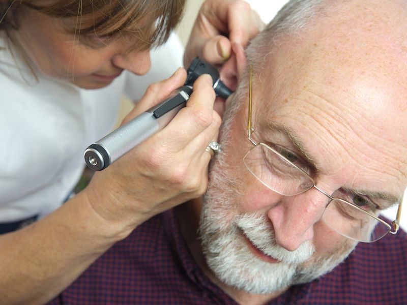 Woman examining older man’s ear with a handheld otoscope