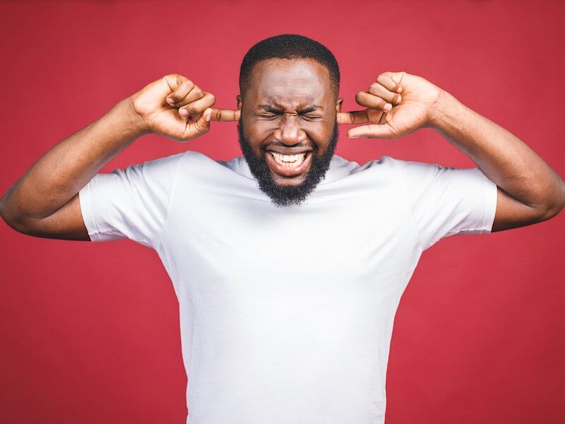 Man in white T-shirt covering his ears and grimacing against a red background