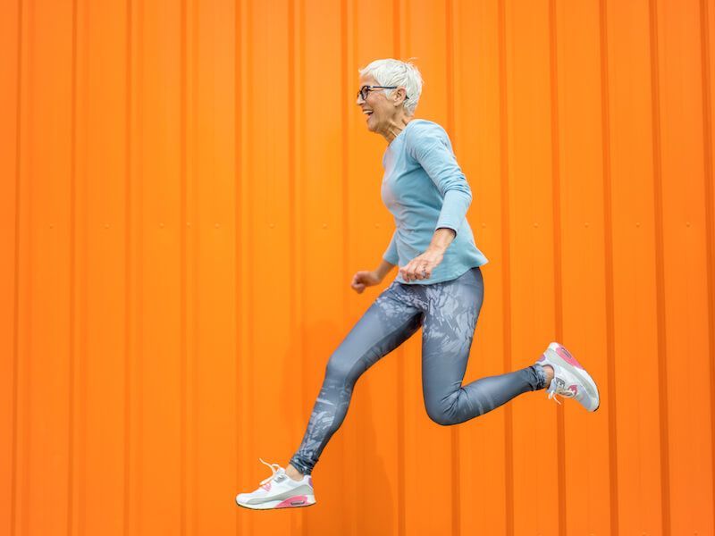 Person running in profile against a bright orange wall, wearing a blue top and jeans