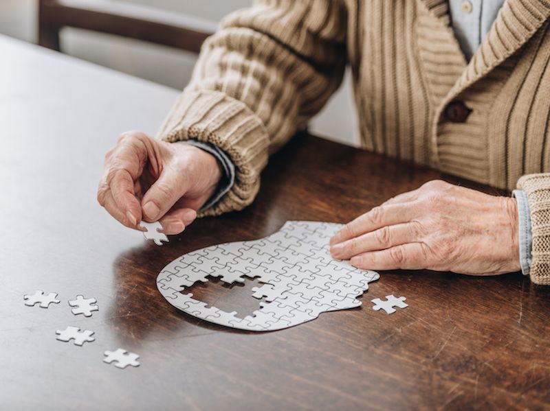 Hands assembling a white jigsaw puzzle on a wooden table with a beige sweater sleeves visible