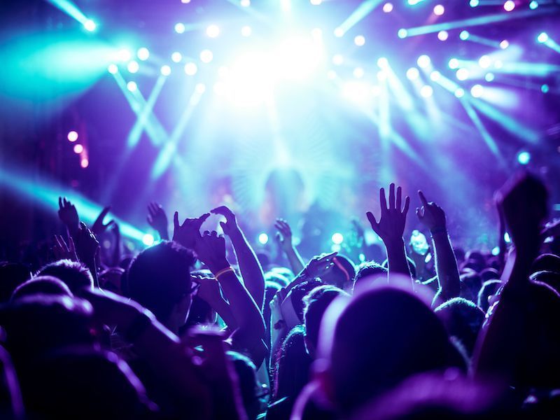 Crowd raising hands at a concert under bright blue and purple stage lights