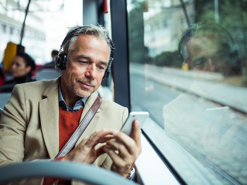 Man in tan blazer using a smartphone on a train, with city buildings visible outside the window