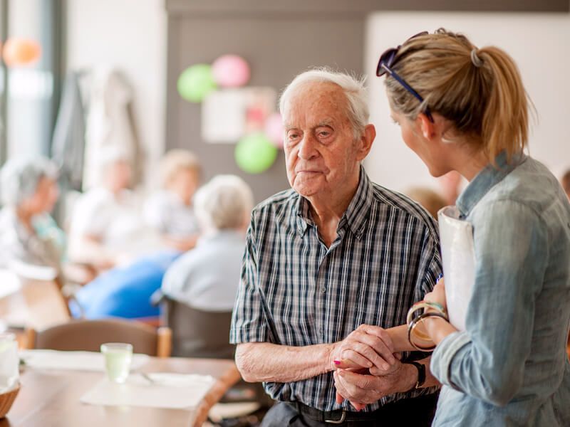 Elderly man and woman talking and holding hands in a bright care facility lounge