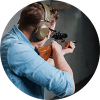 Person aiming a rifle at a target while wearing hearing protection, side view