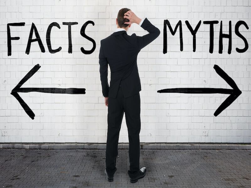 Man in black suit facing a wall labeled “FACTS” and “MYTHS” with arrows pointing left and right