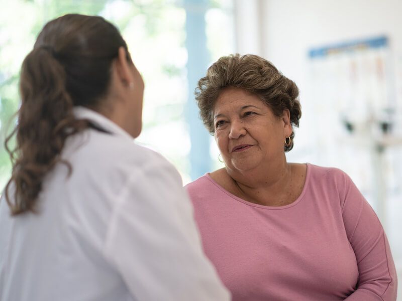 Two women talking in a bright clinic, one in a pink shirt and smiling.