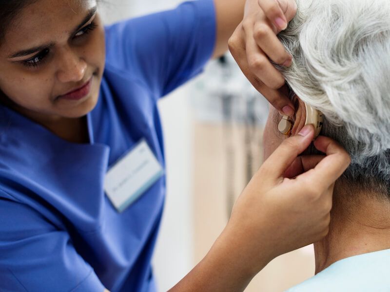 Nurse examining an older patient’s ear with a medical instrument in a clinic