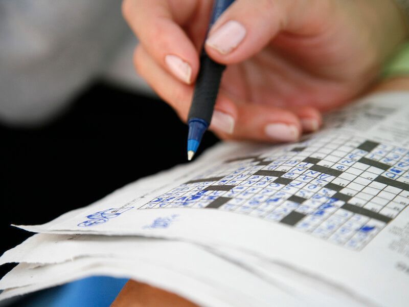 Hand holding a pen over a crossword puzzle on paper