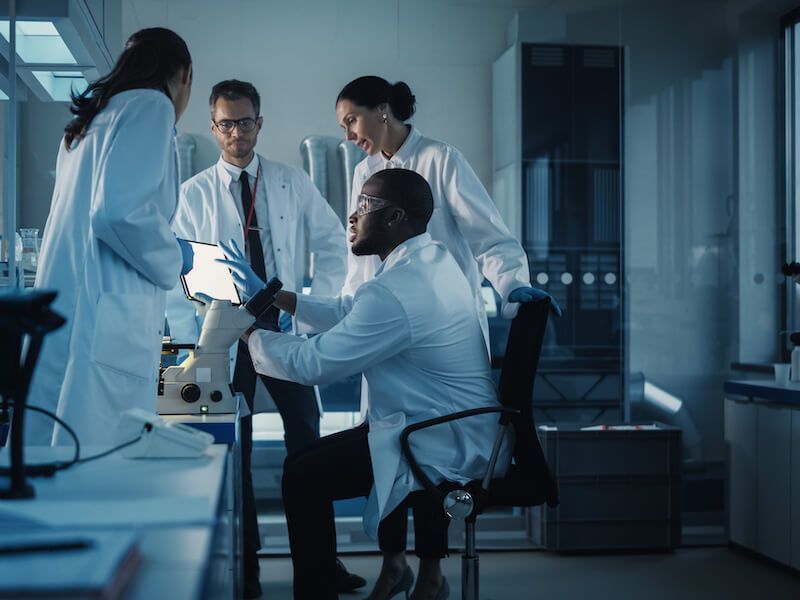 Scientists in lab coats collaborating around a microscope in a dim laboratory