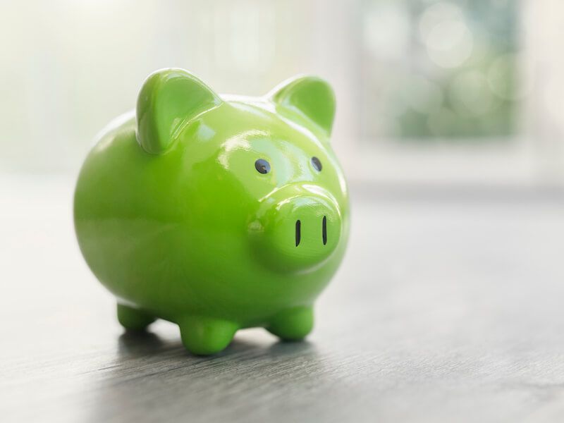Green piggy bank on a tabletop with soft window light in the background