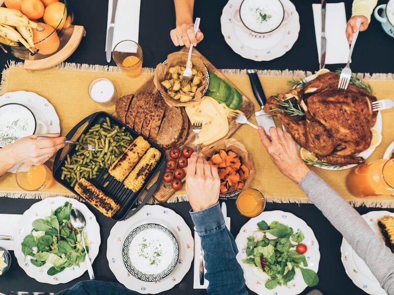 Overhead view of people sharing a colorful meal with grilled food, salad, and drinks at a table