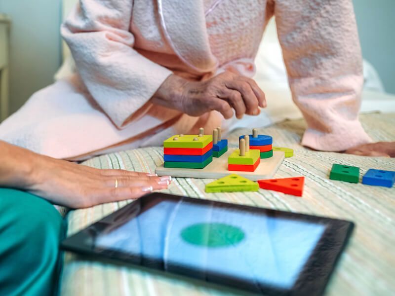 Hands and a tablet on the floor beside colorful stacking blocks and toys
