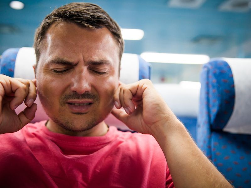 Man on an airplane seat covering his ears with eyes closed, looking uncomfortable