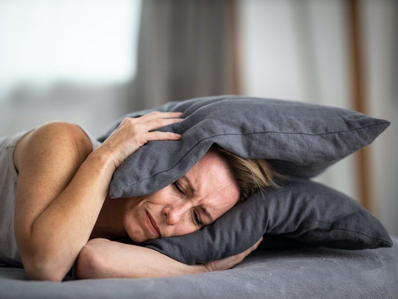Person sleeping on a couch, hugging a gray pillow, with a second pillow under their head.
