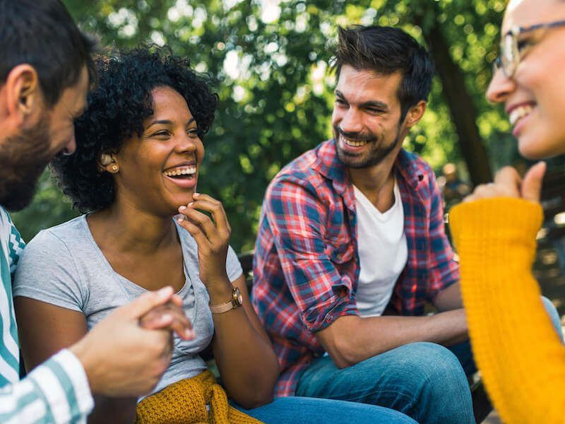 Friends laughing and chatting outdoors in a park, with trees in the background