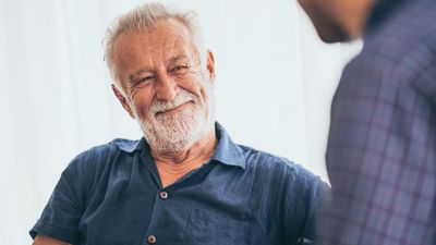 Smiling man in a navy shirt talking with another person in a bright room