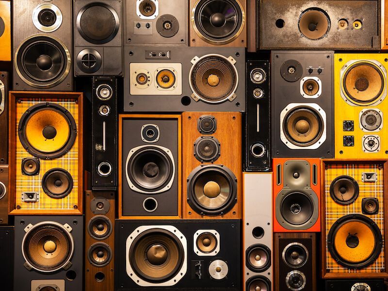 Wall of vintage speakers in varied sizes and colors, tightly stacked in a patterned display
