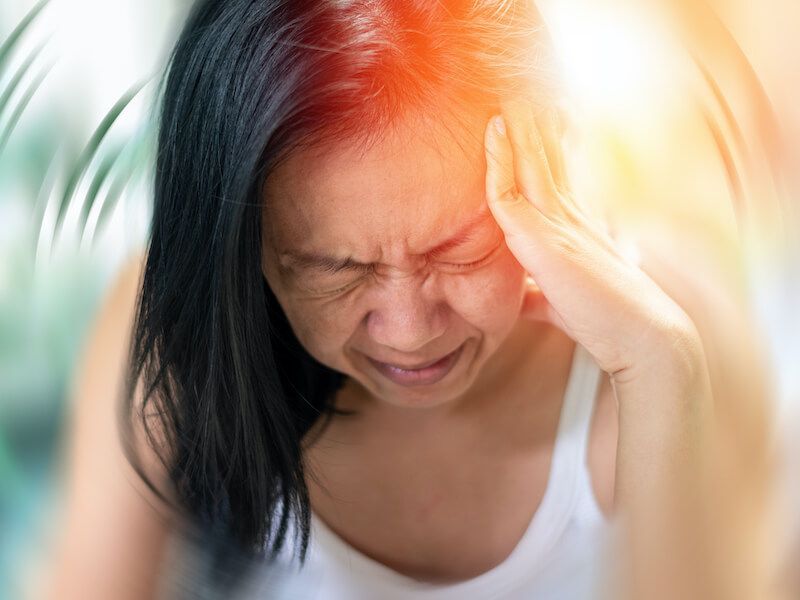 Person holding head in pain with bright light behind them