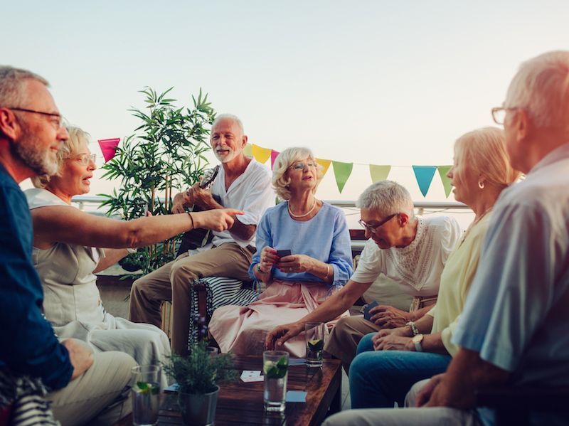 Group of people sitting outdoors on a patio, chatting and sharing drinks around a table at sunset.