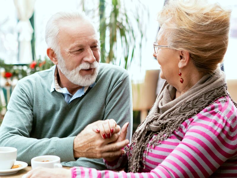 Two people chatting at a café table, holding hands and smiling over coffee.