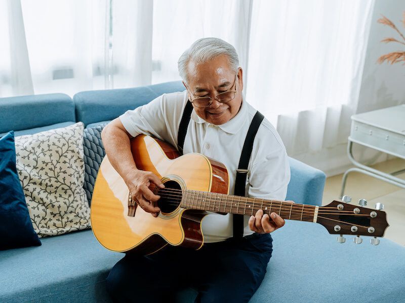 Man playing acoustic guitar on a couch in a bright living room