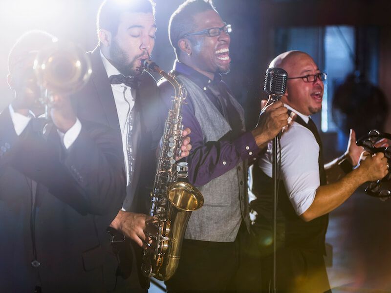 Four musicians performing on stage, including saxophone and brass instruments, under bright stage lights