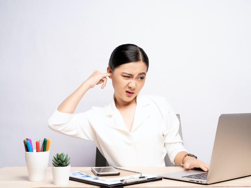Woman at desk, scratching head while looking at a laptop with a puzzled expression.
