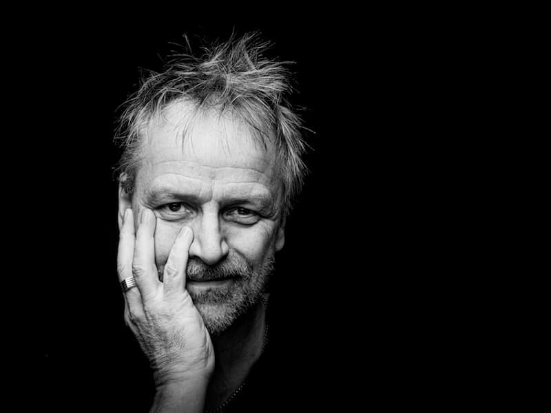 Black-and-white portrait of a man resting his face on his hand against a dark background