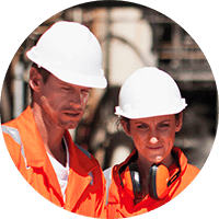 Two construction workers in white hard hats and orange safety vests, looking at plans on a job site