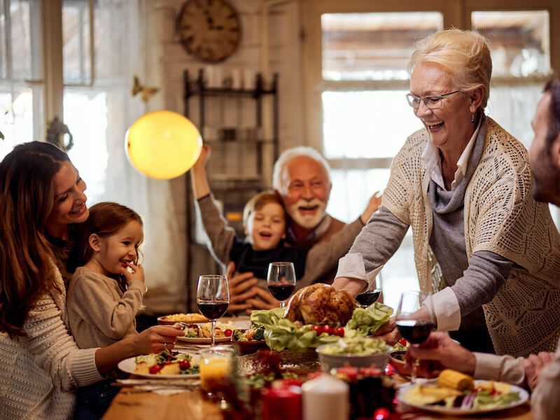 Family gathered around a dinner table as an elderly woman serves a festive meal in a cozy home