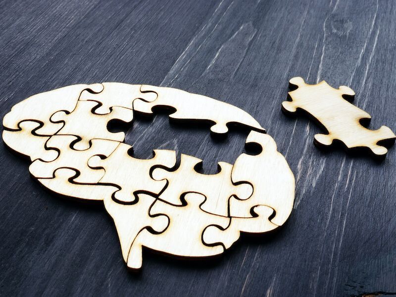 Unfinished white wooden puzzle pieces forming a head silhouette with one piece missing on a dark tabletop