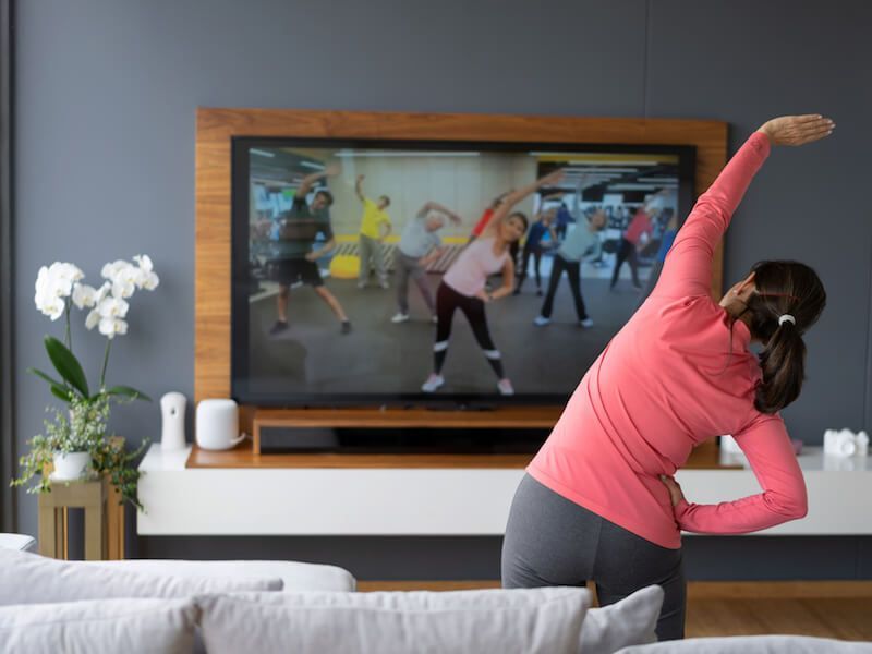 Person stretching in a living room while a TV shows an exercise class.