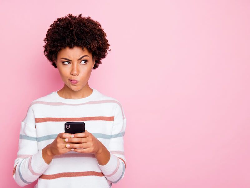 Person in a striped sweater looking down at a phone against a pink background