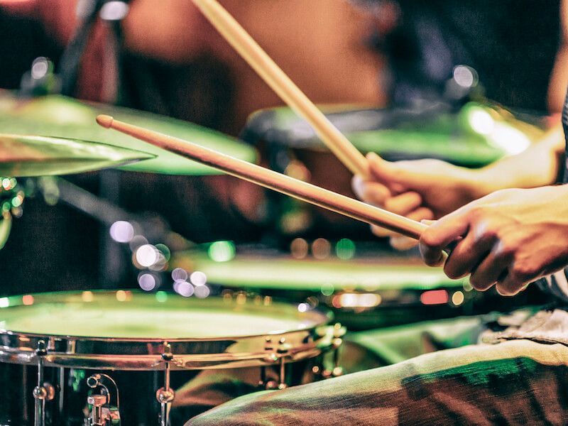Drummer playing a green drum kit with drumsticks in motion on a stage