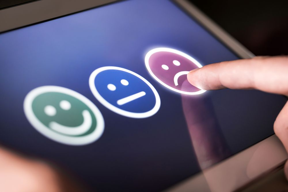 Finger selecting a purple sad face on a tablet with green happy and blue neutral icons