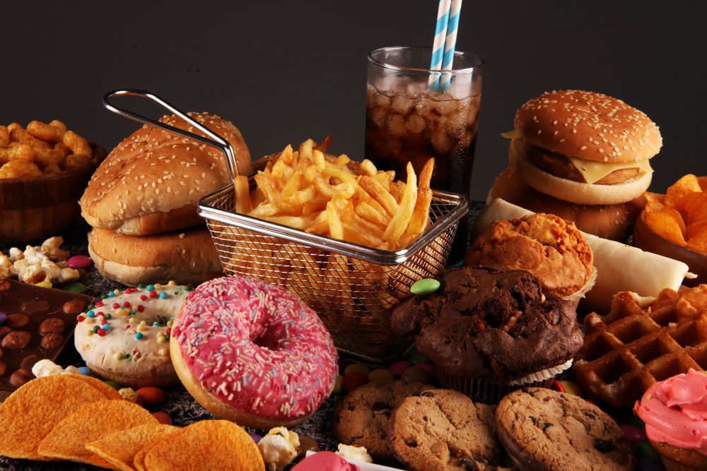 Assorted donuts, fries, burgers, and a soda arranged on a dark table.