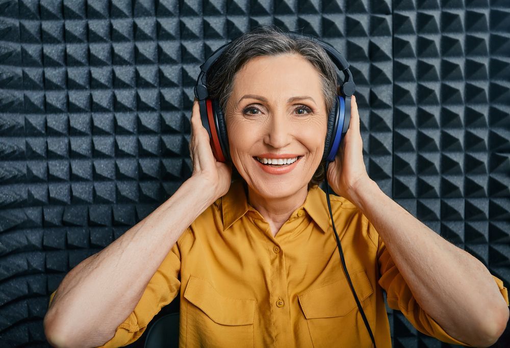 Smiling woman in yellow shirt wearing headphones against a soundproof foam wall