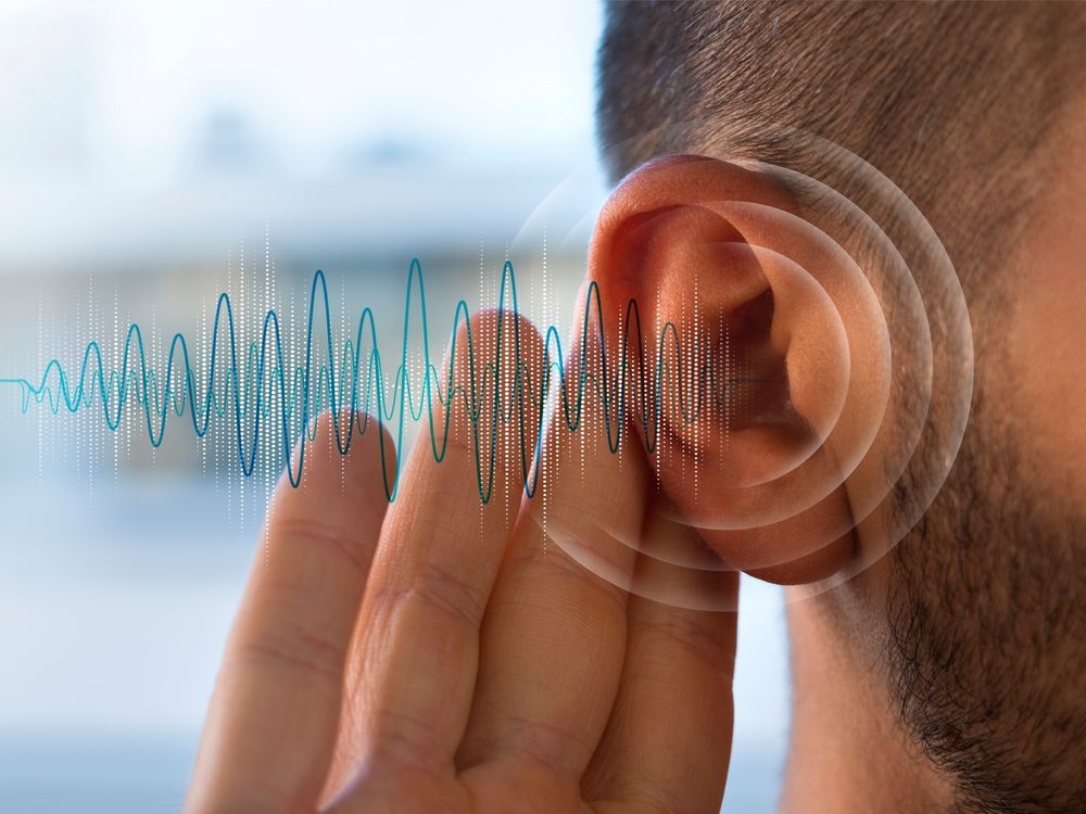 Hand cupped to ear with blue sound waves, suggesting listening or hearing noise