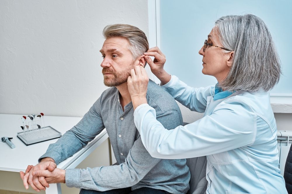 Doctor examining a man’s ear in a clinic, with both seated at a desk